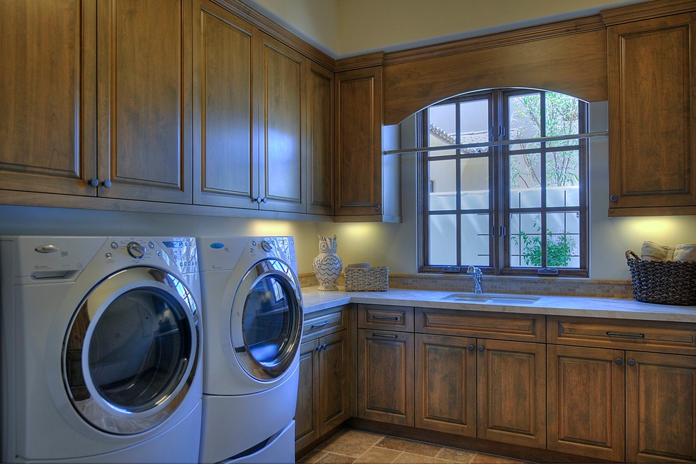 Inspiration för stora klassiska l-formade tvättstugor enbart för tvätt, med en undermonterad diskho, skåp i mellenmörkt trä, beige väggar och en tvättmaskin och torktumlare bredvid varandra