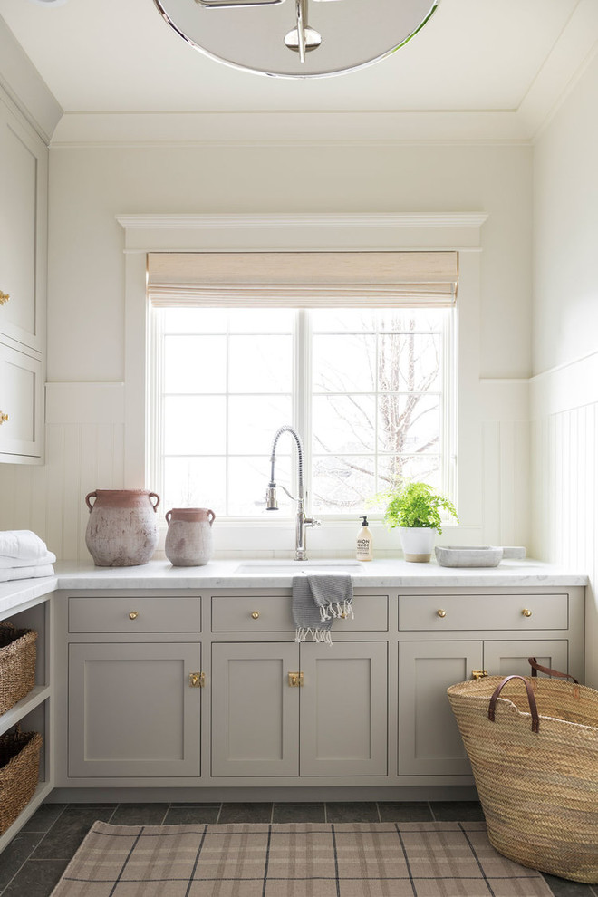 Exempel på en stor maritim flerfärgade l-formad flerfärgat tvättstuga enbart för tvätt, med grå skåp, marmorbänkskiva, vita väggar, klinkergolv i keramik, en tvättmaskin och torktumlare bredvid varandra och grått golv