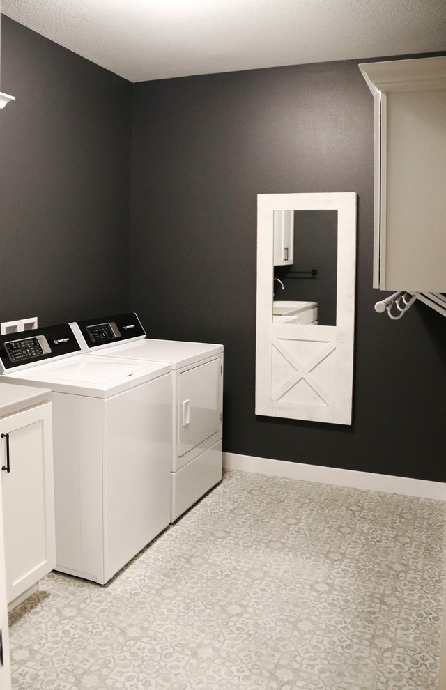 他の地域にある中くらいなトランジショナルスタイルのおしゃれな洗濯室 (ll型、シェーカースタイル扉のキャビネット、白いキャビネット、黒い壁、左右配置の洗濯機・乾燥機、グレーの床、グレーのキッチンカウンター) の写真