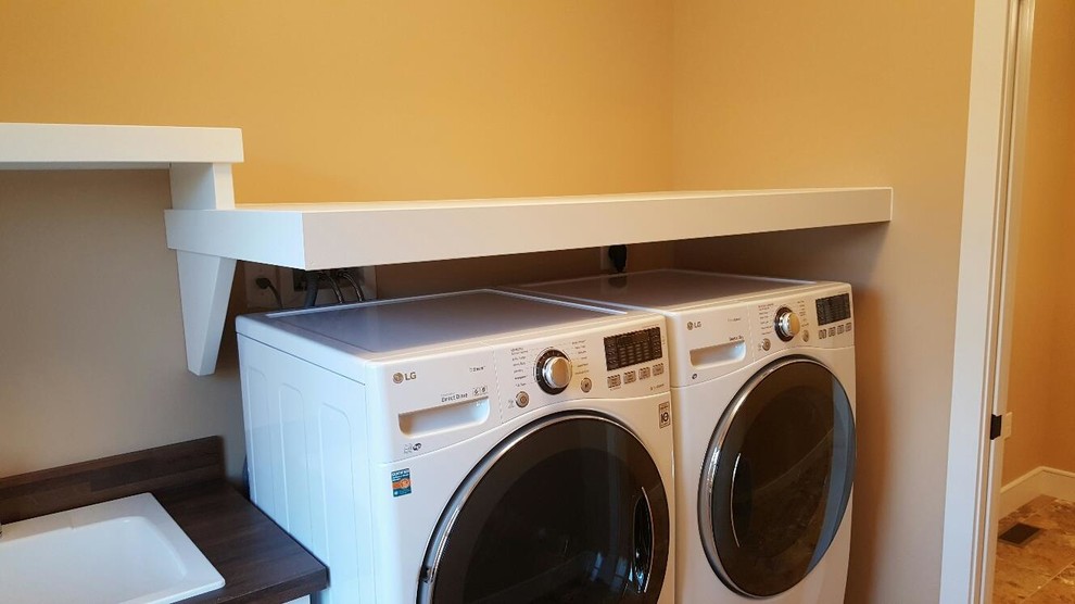 Exempel på en liten amerikansk linjär tvättstuga enbart för tvätt, med öppna hyllor, vita skåp, en tvättmaskin och torktumlare bredvid varandra och orange väggar