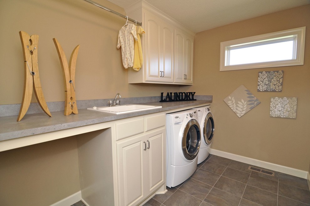 Foto på en amerikansk grå parallell tvättstuga enbart för tvätt, med en nedsänkt diskho, luckor med upphöjd panel, beige skåp, beige väggar, klinkergolv i keramik och en tvättmaskin och torktumlare bredvid varandra