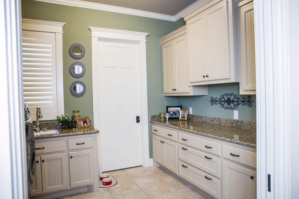Bild på ett parallellt grovkök, med en undermonterad diskho, luckor med profilerade fronter, granitbänkskiva, gröna väggar, klinkergolv i keramik, en tvättmaskin och torktumlare bredvid varandra och vita skåp