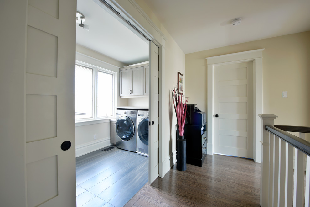 Ejemplo de cuarto de lavado lineal tradicional renovado de tamaño medio con lavadora y secadora juntas, armarios estilo shaker, puertas de armario blancas y paredes amarillas