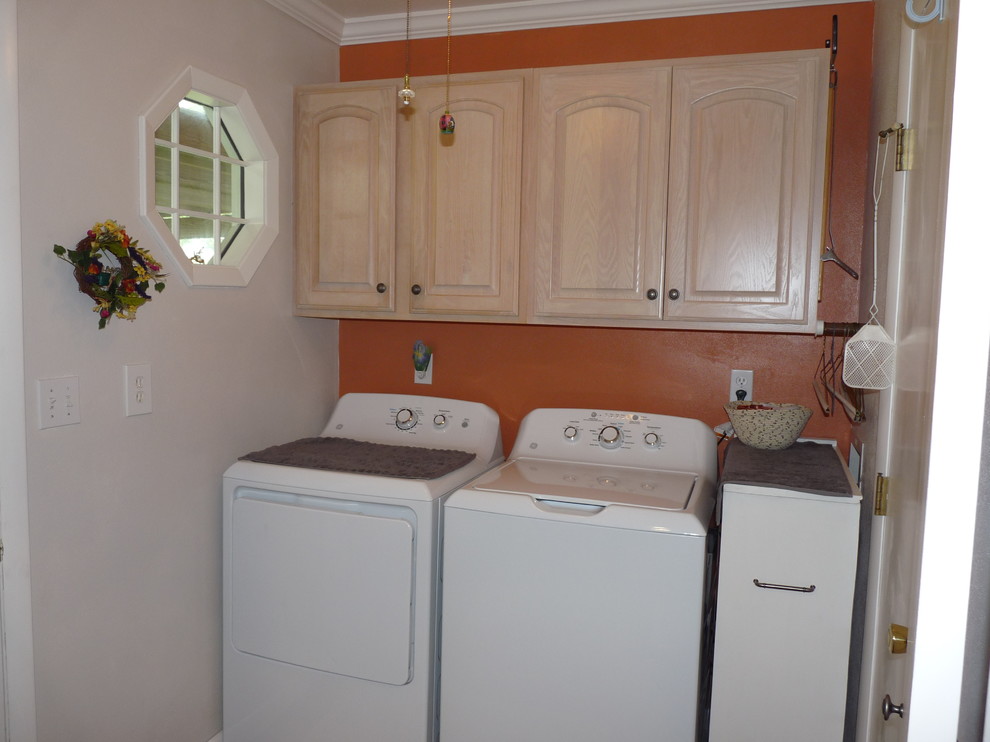 Idee per una piccola sala lavanderia tradizionale con ante con bugna sagomata, ante in legno chiaro, pareti arancioni, pavimento in vinile e lavatrice e asciugatrice affiancate