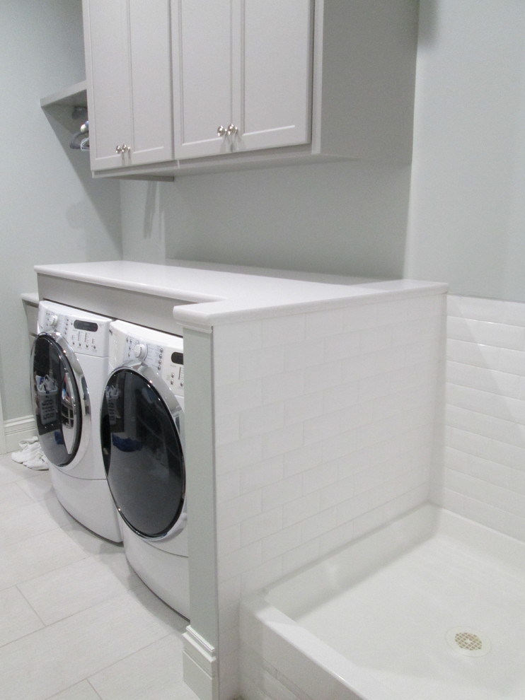 Photo of a medium sized classic single-wall utility room in St Louis with an utility sink, recessed-panel cabinets, white cabinets, composite countertops, grey walls, porcelain flooring, a side by side washer and dryer and white floors.
