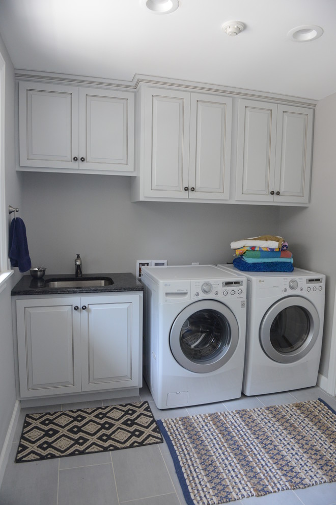 Immagine di una lavanderia costiera di medie dimensioni con lavello sottopiano, ante bianche, top in granito, pareti grigie, pavimento con piastrelle in ceramica e lavatrice e asciugatrice affiancate