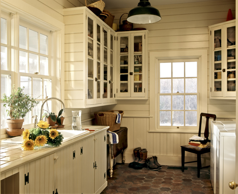 Inspiration for a farmhouse utility room remodel in New York with a drop-in sink, glass-front cabinets, white cabinets, tile countertops, white walls and a side-by-side washer/dryer