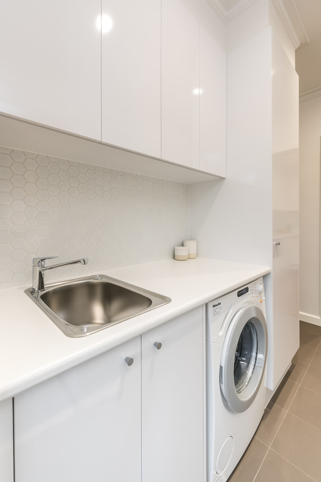 Exempel på en liten modern linjär tvättstuga enbart för tvätt, med en enkel diskho, vita skåp, laminatbänkskiva, vita väggar, klinkergolv i keramik och en tvättmaskin och torktumlare bredvid varandra