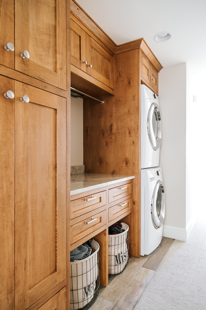 Photo of a medium sized traditional single-wall utility room in Minneapolis with shaker cabinets, medium wood cabinets, quartz worktops, beige walls, ceramic flooring, a stacked washer and dryer and beige floors.