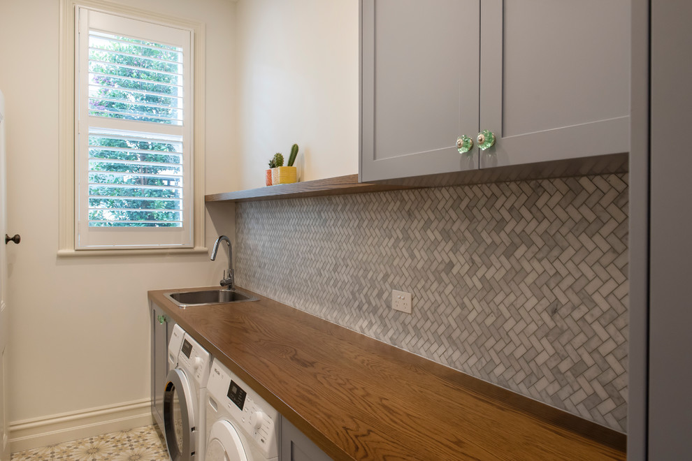 Photo of a large mediterranean single-wall separated utility room in Melbourne with a built-in sink, shaker cabinets, grey cabinets, wood worktops, white walls, ceramic flooring, a side by side washer and dryer and yellow floors.