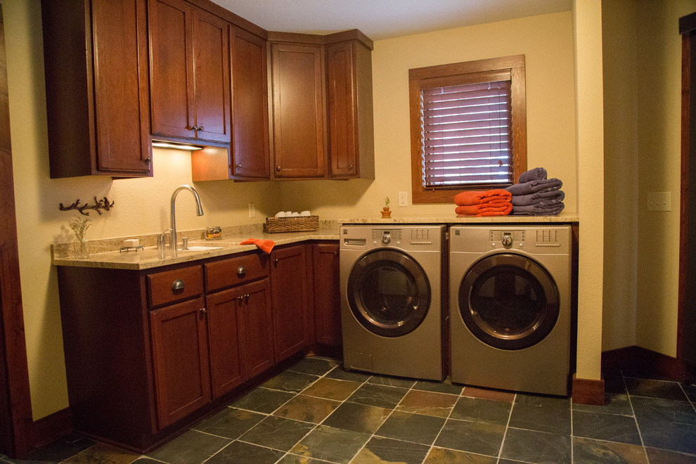 Rustikale Waschküche mit Unterbauwaschbecken, Schrankfronten mit vertiefter Füllung, hellbraunen Holzschränken, Granit-Arbeitsplatte, Schieferboden und Waschmaschine und Trockner nebeneinander in Minneapolis