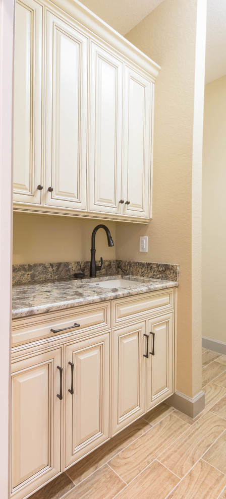 Exempel på en mellanstor klassisk parallell tvättstuga enbart för tvätt, med en undermonterad diskho, luckor med upphöjd panel, beige skåp, granitbänkskiva, beige väggar, klinkergolv i porslin, en tvättpelare och brunt golv