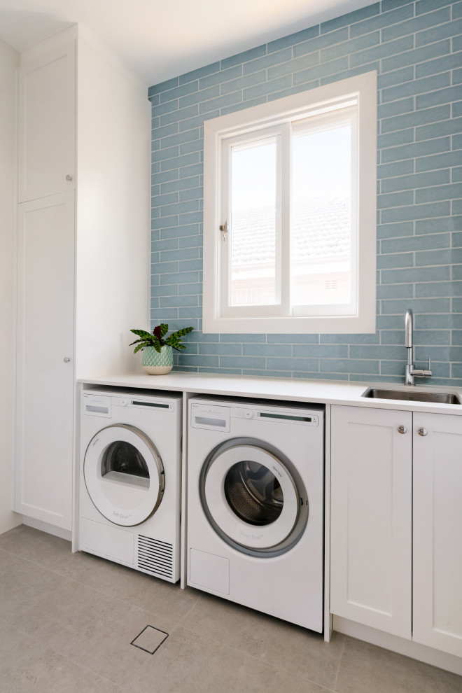 Photo of a traditional single-wall utility room in Sydney with a submerged sink, shaker cabinets, white cabinets, engineered stone countertops, metro tiled splashback, porcelain flooring, a side by side washer and dryer, grey floors and white worktops.