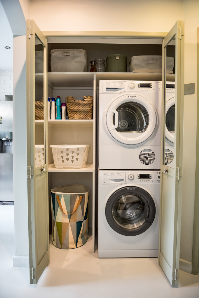 Imagen de armario lavadero lineal bohemio pequeño con armarios abiertos, paredes blancas, suelo de cemento, lavadora y secadora apiladas, suelo blanco y encimeras blancas