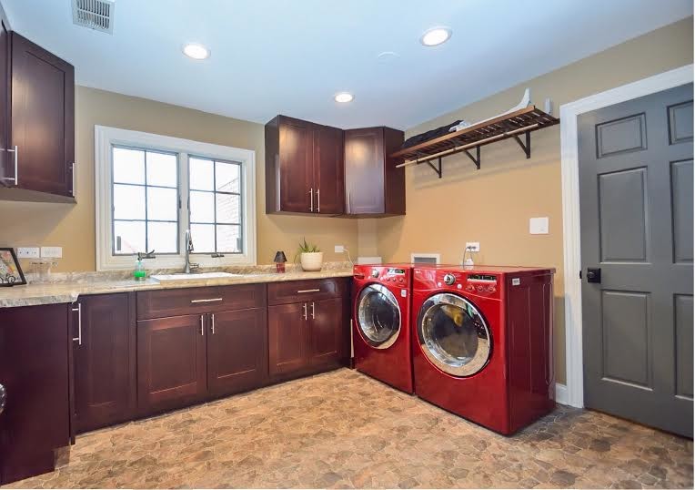 Photo of a large classic u-shaped utility room in Chicago with an utility sink, shaker cabinets, dark wood cabinets, granite worktops, brown walls, porcelain flooring, a side by side washer and dryer and beige floors.