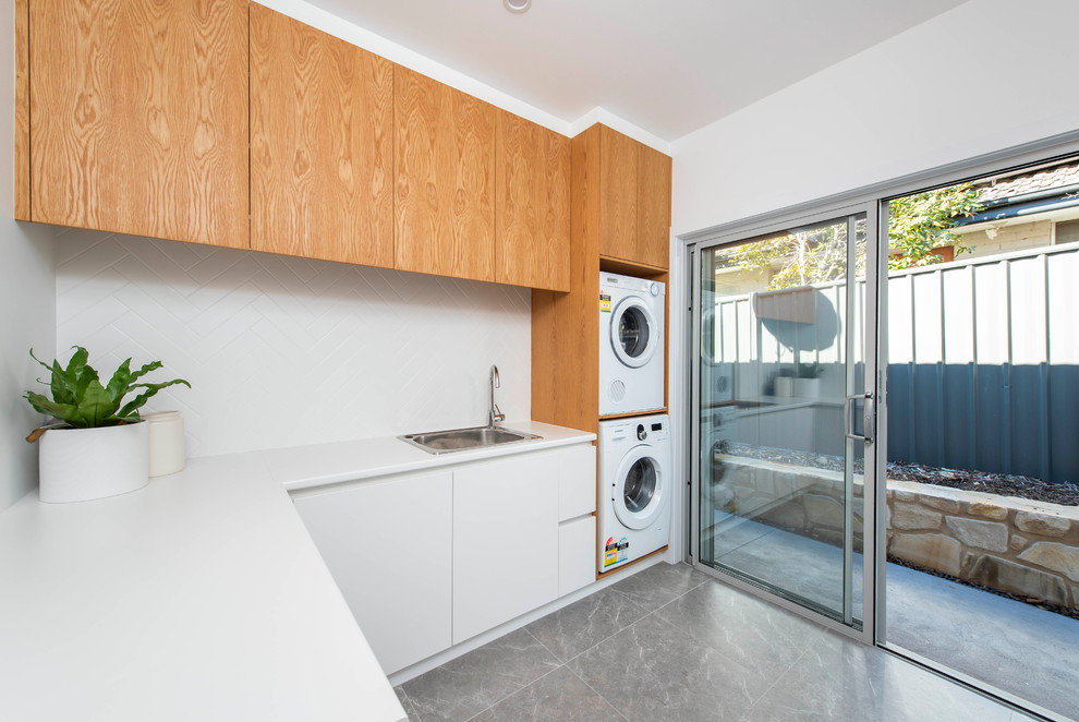 Design ideas for a contemporary l-shaped utility room in Canberra - Queanbeyan with a built-in sink, flat-panel cabinets, white cabinets, white walls, a stacked washer and dryer, grey floors and white worktops.