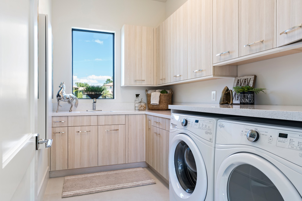 Exempel på en modern grå l-formad grått tvättstuga enbart för tvätt, med en undermonterad diskho, släta luckor, bruna skåp, vita väggar, en tvättmaskin och torktumlare bredvid varandra och beiget golv