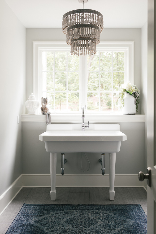 Exempel på en stor klassisk linjär tvättstuga enbart för tvätt, med en allbänk, bänkskiva i koppar, grå väggar, mellanmörkt trägolv, en tvättmaskin och torktumlare bredvid varandra och grått golv