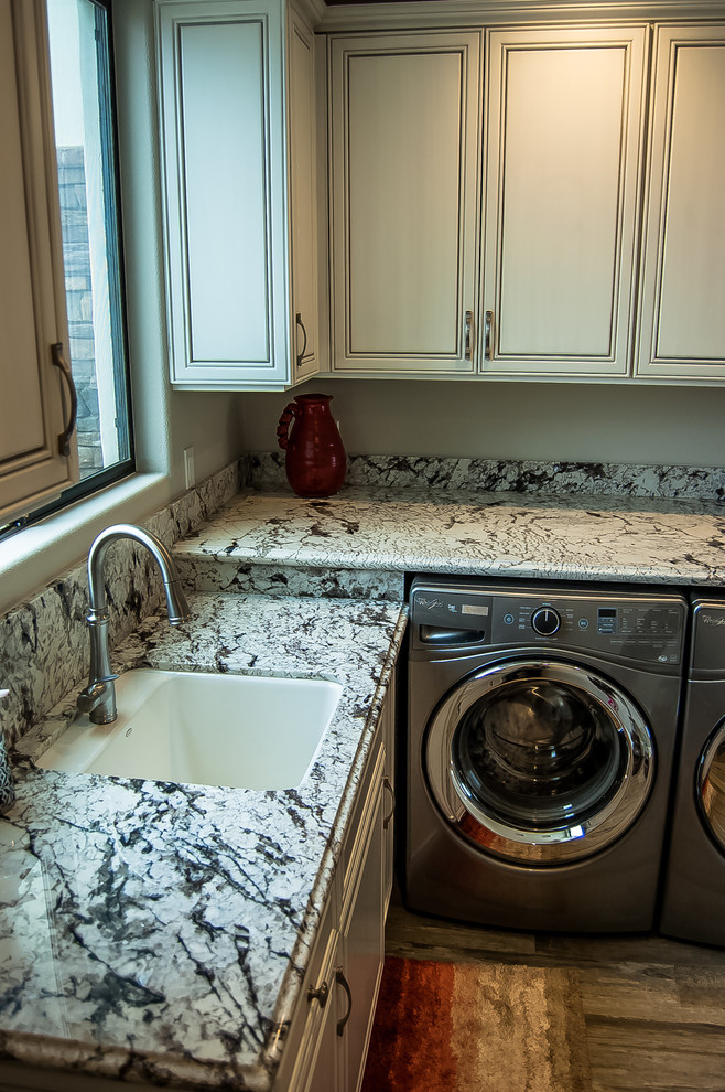 Mittelgroße Klassische Waschküche in L-Form mit Unterbauwaschbecken, profilierten Schrankfronten, weißen Schränken, Granit-Arbeitsplatte, grauer Wandfarbe, braunem Holzboden, Waschmaschine und Trockner nebeneinander und braunem Boden in Los Angeles