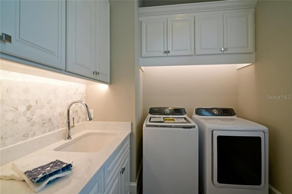 Modelo de cuarto de lavado costero con puertas de armario blancas, paredes beige, lavadora y secadora juntas y encimeras blancas