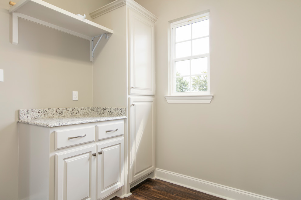 Inredning av en klassisk mellanstor vita linjär vitt tvättstuga enbart för tvätt, med luckor med upphöjd panel, grå skåp, granitbänkskiva, grå väggar, vinylgolv, en tvättmaskin och torktumlare bredvid varandra och brunt golv