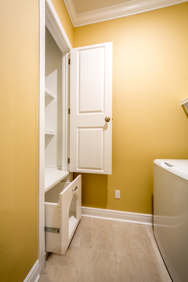 ジャクソンビルにあるお手頃価格の中くらいなトラディショナルスタイルのおしゃれな洗濯室 (I型、レイズドパネル扉のキャビネット、白いキャビネット、黄色い壁、セラミックタイルの床、左右配置の洗濯機・乾燥機、ベージュの床) の写真