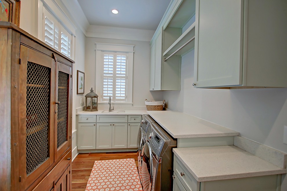 Photo of a medium sized traditional galley separated utility room in Charleston with a submerged sink, shaker cabinets, green cabinets, engineered stone countertops, white walls, medium hardwood flooring and a side by side washer and dryer.