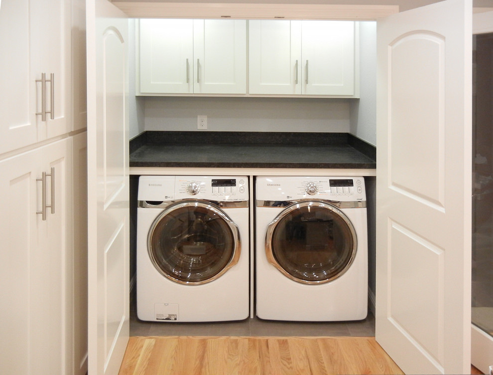 Medium sized classic single-wall laundry cupboard with shaker cabinets, white cabinets, soapstone worktops and a side by side washer and dryer.
