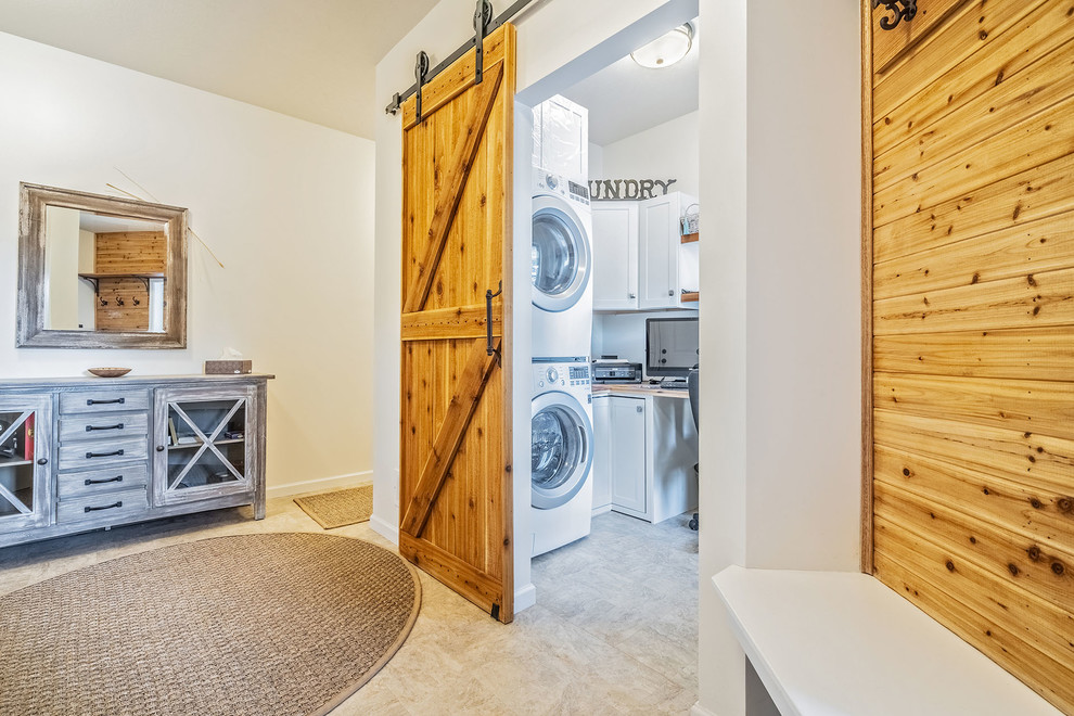 Example of a large cottage l-shaped ceramic tile and multicolored floor utility room design in New York with shaker cabinets, white cabinets, wood countertops, white walls and a stacked washer/dryer