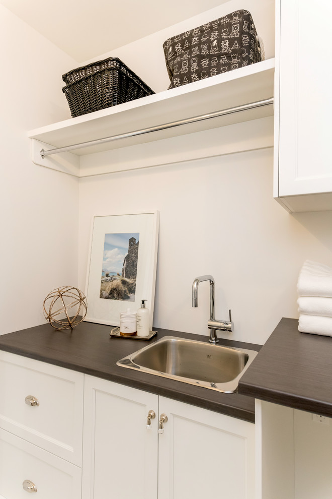 Exempel på en liten klassisk linjär tvättstuga enbart för tvätt, med en nedsänkt diskho, skåp i shakerstil, vita skåp, laminatbänkskiva, vita väggar, en tvättmaskin och torktumlare bredvid varandra, marmorgolv och vitt golv