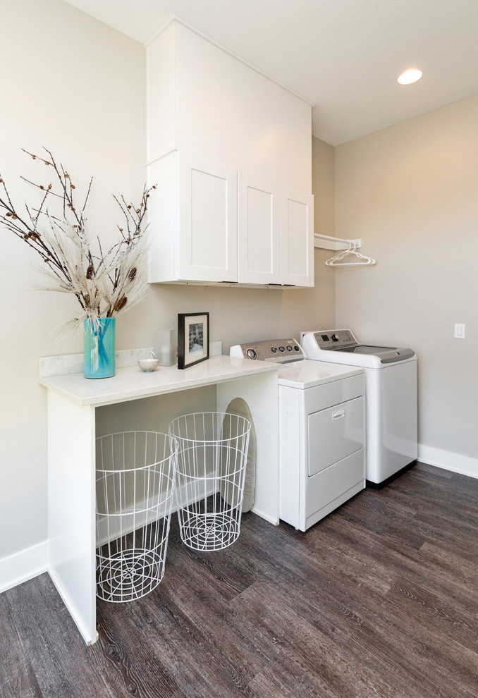 Ejemplo de cuarto de lavado lineal actual con paredes grises, suelo de madera en tonos medios, lavadora y secadora juntas, armarios estilo shaker, puertas de armario blancas y encimeras blancas