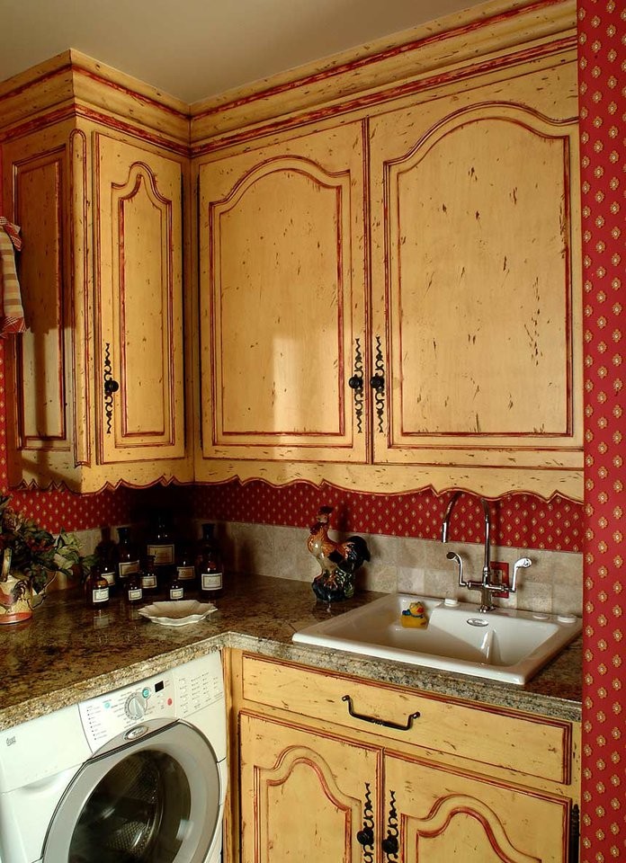 Cette image montre une buanderie traditionnelle avec un évier posé, un placard avec porte à panneau surélevé, des portes de placard jaunes, un plan de travail en granite et un mur rouge.