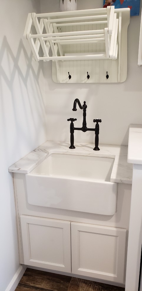 Design ideas for a large galley separated utility room in Detroit with a belfast sink, recessed-panel cabinets, white cabinets, marble worktops, white walls, porcelain flooring, an integrated washer and dryer, brown floors and white worktops.