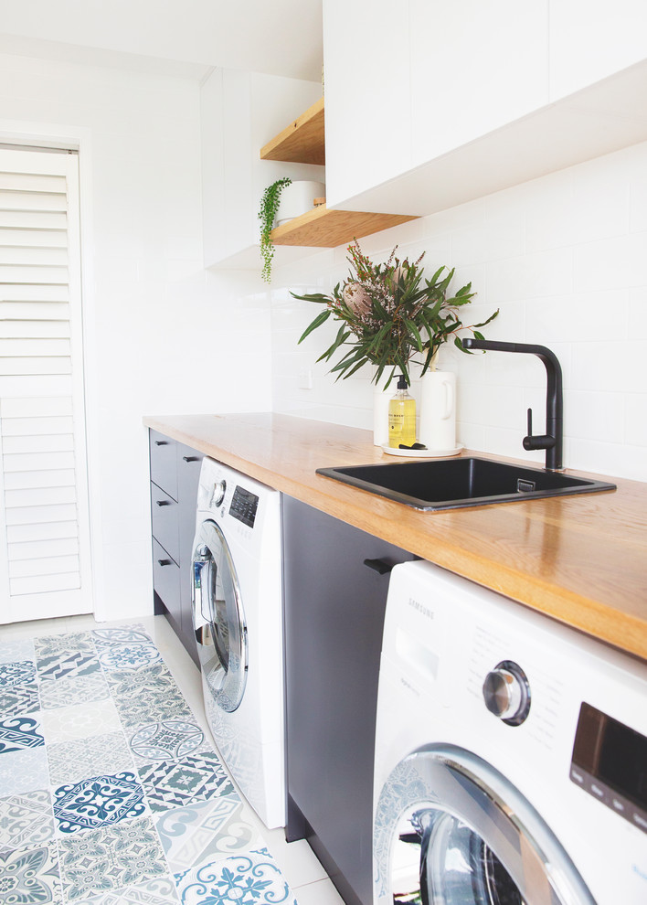 Diseño de lavadero minimalista con fregadero encastrado, paredes blancas, suelo vinílico y lavadora y secadora juntas