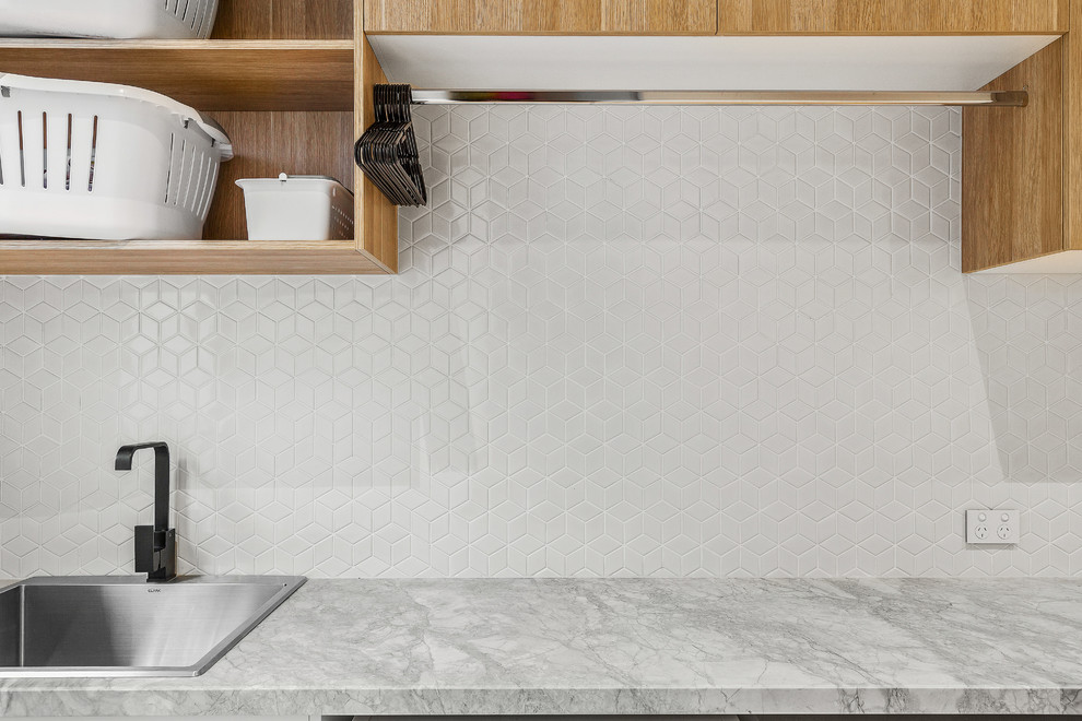 Einzeilige, Große Moderne Waschküche mit Waschbecken, weißen Schränken, Marmor-Arbeitsplatte, weißer Wandfarbe, hellem Holzboden, Waschmaschine und Trockner nebeneinander und grauer Arbeitsplatte in Melbourne