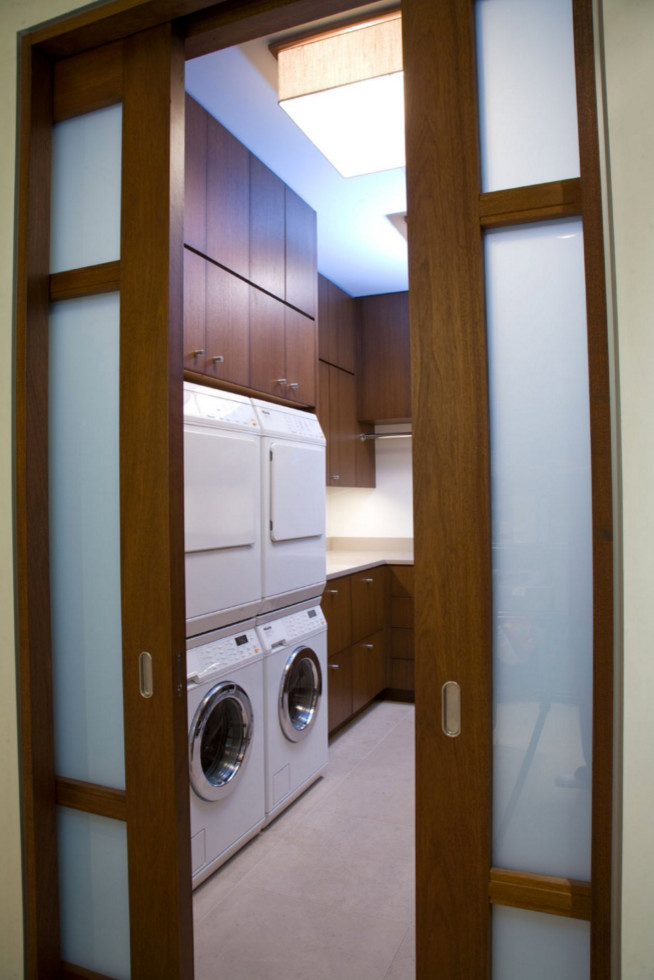 Ejemplo de lavadero en L actual grande con armarios con paneles lisos, puertas de armario de madera oscura, paredes blancas y lavadora y secadora apiladas