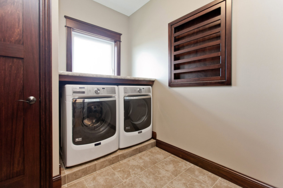 Example of a small classic single-wall travertine floor and beige floor dedicated laundry room design in Cedar Rapids with dark wood cabinets, granite countertops, beige walls and a side-by-side washer/dryer