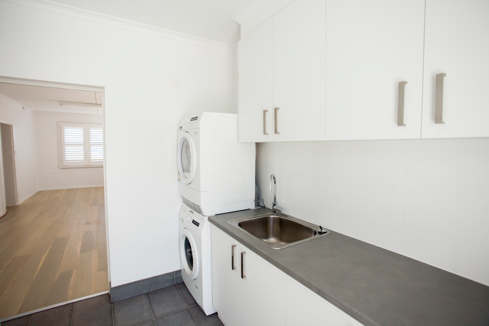 Ispirazione per una sala lavanderia minimalista con lavello da incasso, ante lisce, ante bianche, pareti bianche, top in laminato, lavatrice e asciugatrice a colonna e pavimento grigio