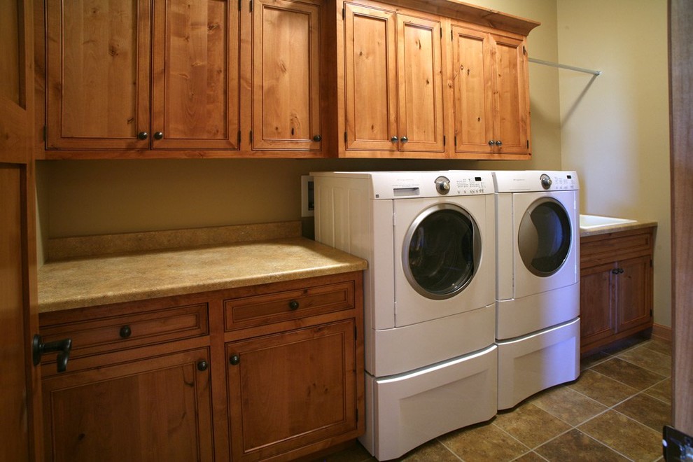Diseño de lavadero tradicional con puertas de armario de madera oscura, paredes beige y lavadora y secadora juntas
