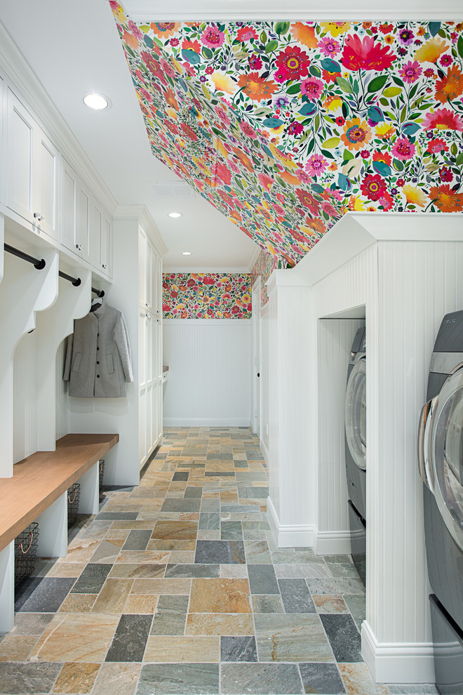 Lantlig inredning av ett stort parallellt grovkök, med vita skåp, vita väggar, en tvättmaskin och torktumlare bredvid varandra, flerfärgat golv och skåp i shakerstil
