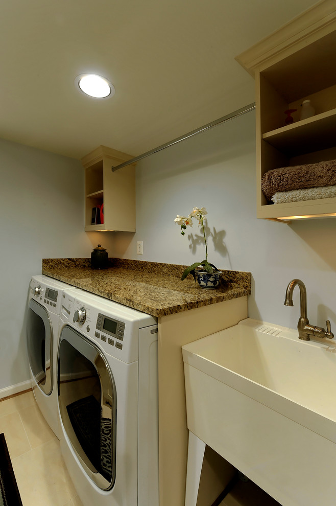 Klassisk inredning av en mellanstor tvättstuga, med en allbänk, öppna hyllor, granitbänkskiva, grå väggar, en tvättmaskin och torktumlare bredvid varandra och beiget golv