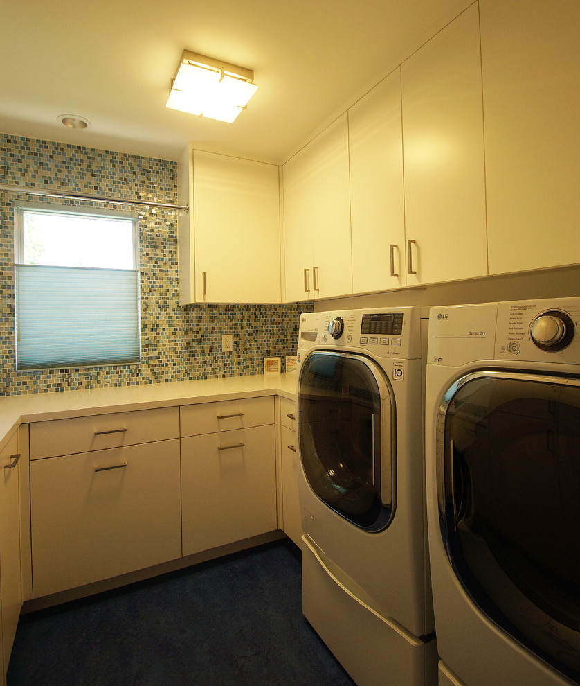 Foto på en stor funkis vita u-formad tvättstuga enbart för tvätt, med släta luckor, vita skåp, bänkskiva i kvarts, flerfärgade väggar, linoleumgolv, en tvättmaskin och torktumlare bredvid varandra och blått golv