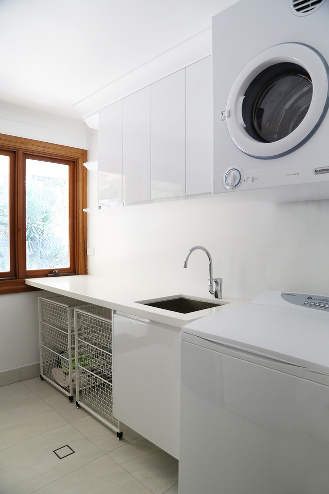 Foto de cuarto de lavado lineal actual de tamaño medio con fregadero bajoencimera, armarios con paneles lisos, puertas de armario blancas y encimeras blancas