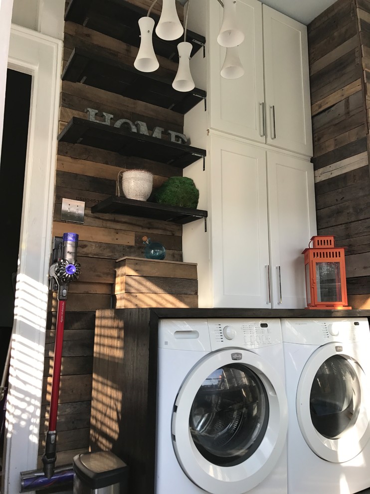 Foto de cuarto de lavado lineal rural pequeño con armarios estilo shaker, puertas de armario blancas, encimera de madera, paredes grises, suelo de cemento, lavadora y secadora juntas y suelo gris