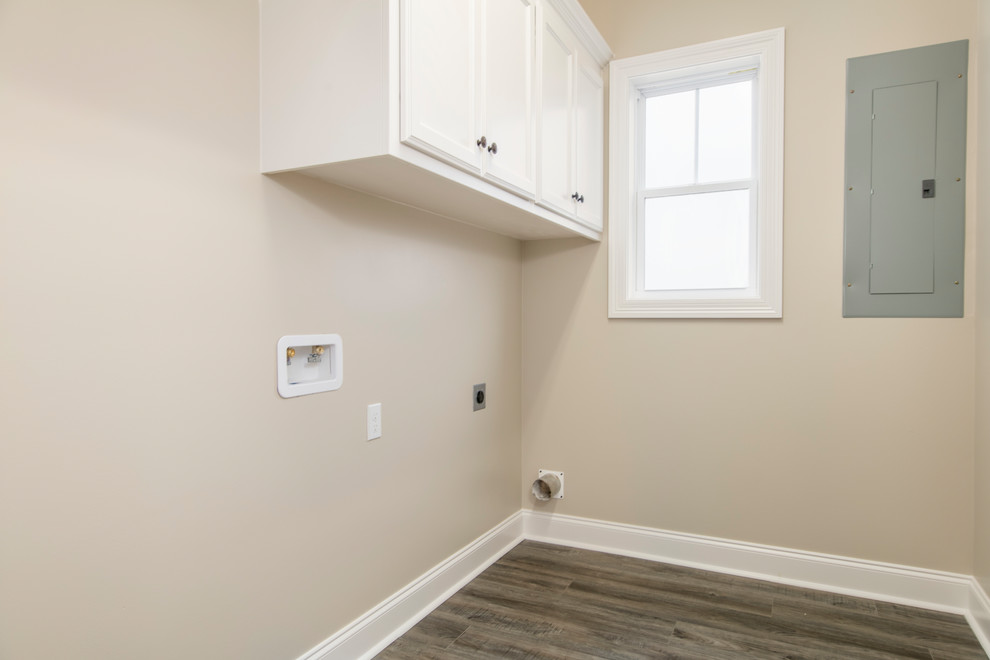Bild på en mellanstor lantlig linjär tvättstuga enbart för tvätt, med släta luckor, vita skåp, beige väggar, en tvättmaskin och torktumlare bredvid varandra, brunt golv och vinylgolv