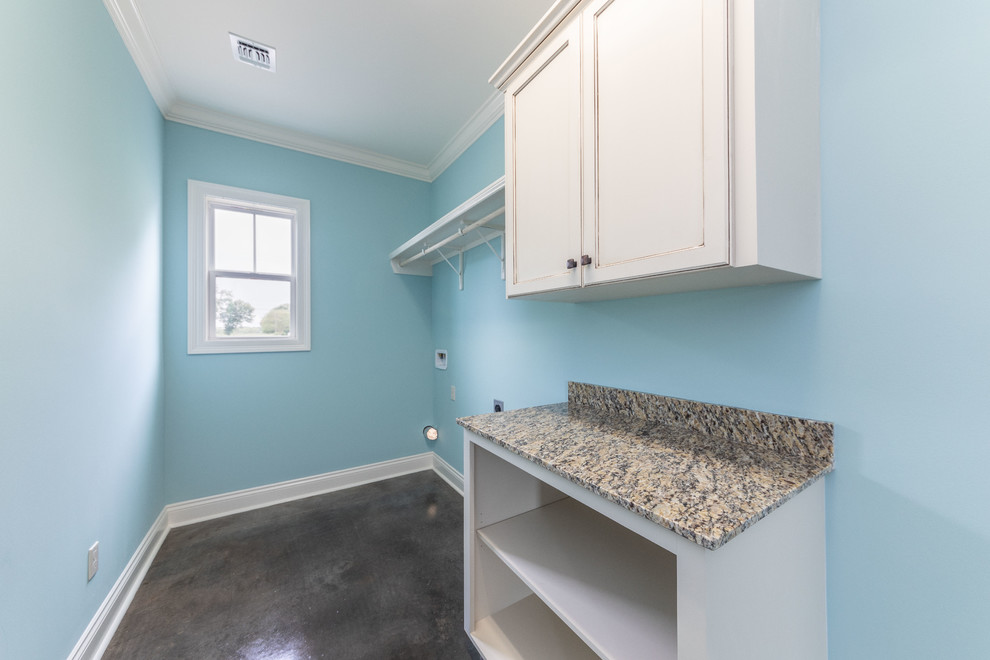 Idéer för att renovera en mellanstor lantlig beige linjär beige tvättstuga enbart för tvätt, med släta luckor, vita skåp, granitbänkskiva, blå väggar, betonggolv, en tvättmaskin och torktumlare bredvid varandra och brunt golv