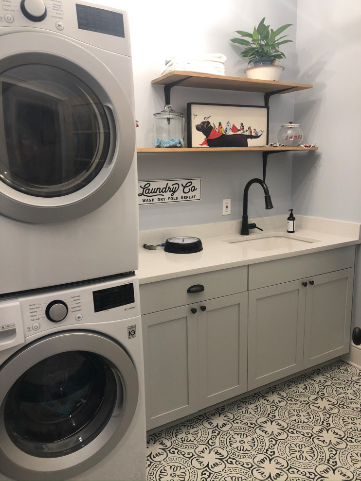 Photo of a rural utility room in Charlotte with an utility sink, shaker cabinets, grey cabinets, engineered stone countertops, ceramic flooring, a stacked washer and dryer and white worktops.