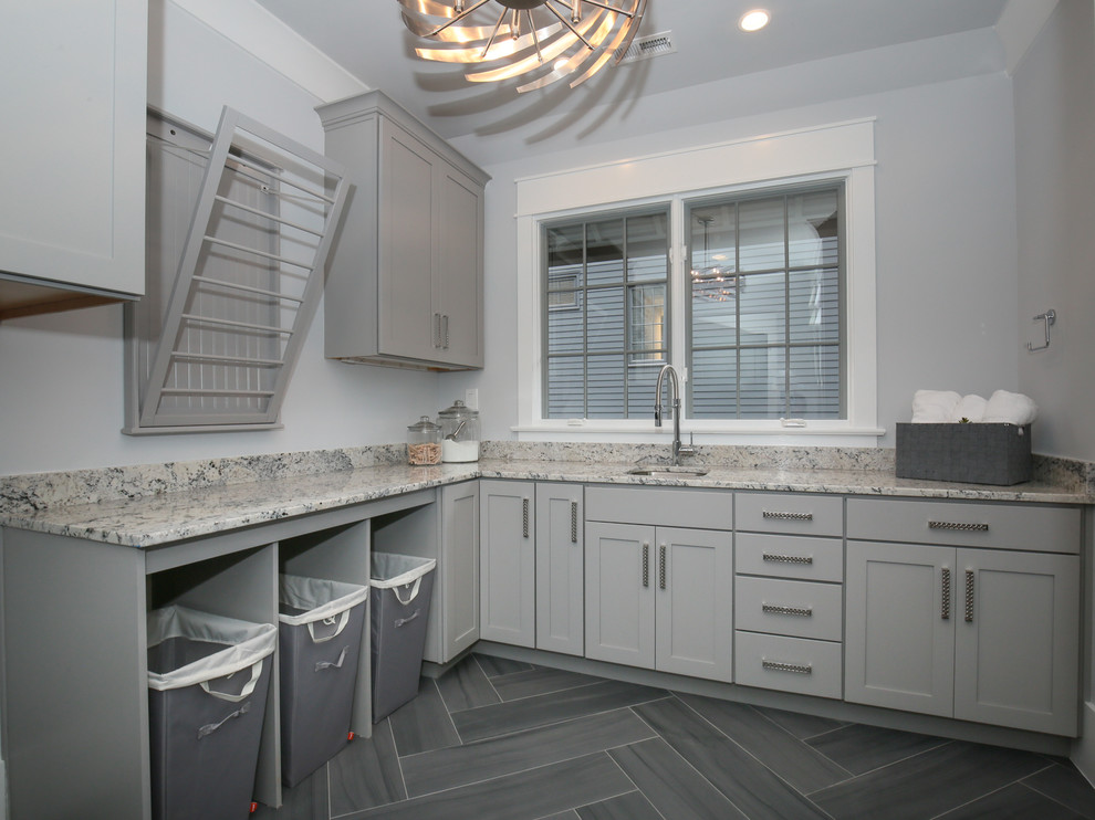 Inspiration for a large transitional l-shaped porcelain tile and gray floor dedicated laundry room remodel in Raleigh with an undermount sink, shaker cabinets, gray cabinets, granite countertops, gray walls, a side-by-side washer/dryer and multicolored countertops