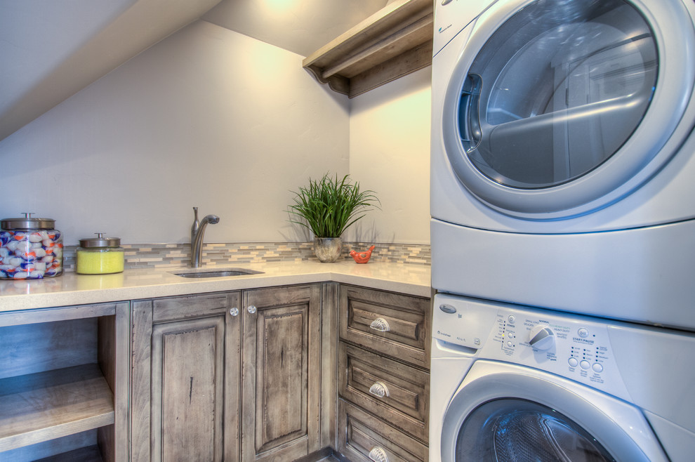 Kleine Klassische Waschküche in L-Form mit Unterbauwaschbecken, profilierten Schrankfronten, Quarzwerkstein-Arbeitsplatte, grauer Wandfarbe, gebeiztem Holzboden, Waschmaschine und Trockner gestapelt und grauen Schränken in Salt Lake City
