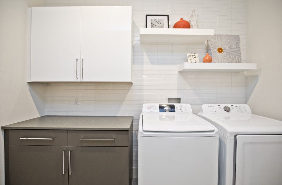 Foto på en funkis grå linjär tvättstuga, med släta luckor, vita skåp, vita väggar och en tvättmaskin och torktumlare bredvid varandra